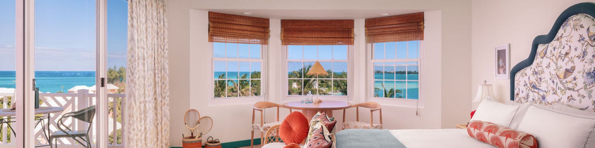 A bright, airy bedroom with sea view, large windows, a balcony, tropical decor, and a cozy sitting area.