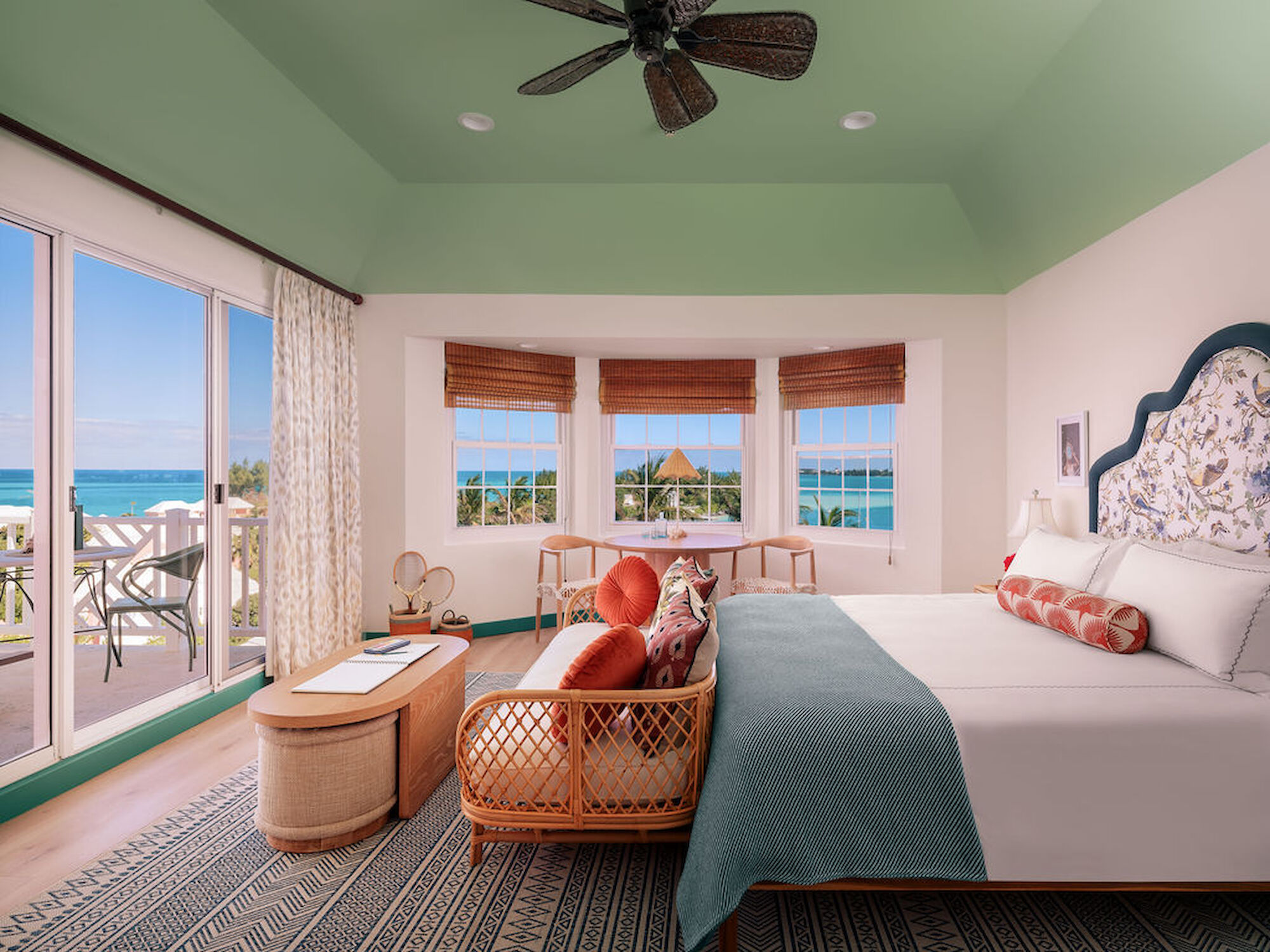 A bright, airy bedroom with sea view, large windows, a balcony, tropical decor, and a cozy sitting area.