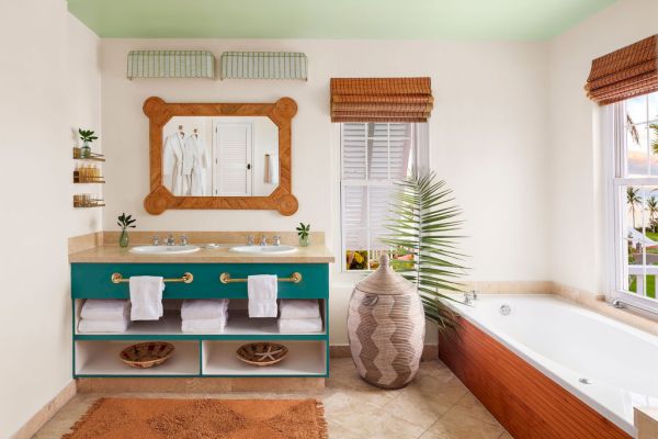 The image shows a stylish bathroom with a double sink vanity, a large mirror, and a bathtub. There are potted plants and natural light from windows.
