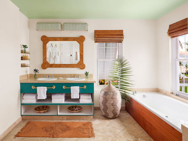 The image shows a stylish bathroom with a double sink vanity, a large mirror, and a bathtub. There are potted plants and natural light from windows.