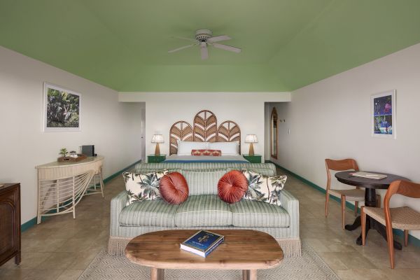 A cozy living room with a sofa, coffee table, bed, two lamps, a small desk, and chairs, decorated with vibrant cushions and wall art, ends the sentence.