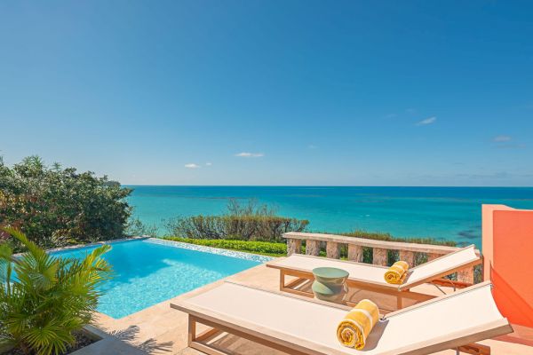 An ocean view from a poolside deck with two lounge chairs, towels, plants, and a clear blue sky in the background, creating a serene atmosphere.