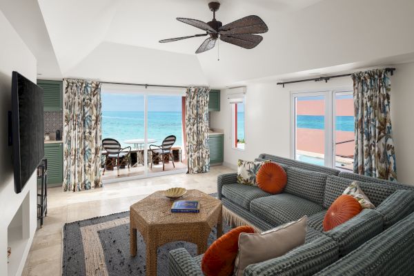 A spacious living room with wicker furniture, ocean-themed decor, and large windows revealing a stunning ocean view. Ends with a complete sentence.