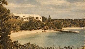 A tropical coastline with a sandy beach, palm trees, and white seaside houses rising above the shore, calm blue water, and a small pier.
