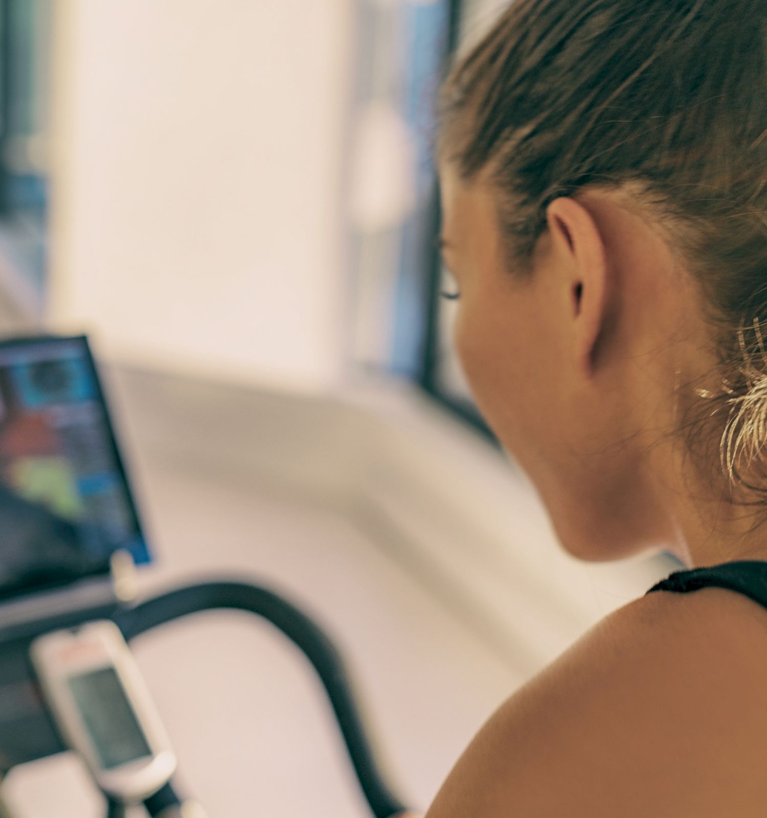 A person is using a stationary bike, watching a screen that likely displays a virtual road or biking program, in a sunlit indoor space.