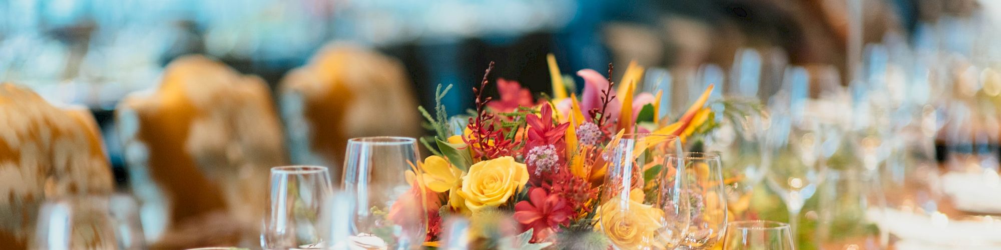 The image shows an elegantly set dining table with plates, wine glasses, and a vibrant floral centerpiece, ready for a formal meal.