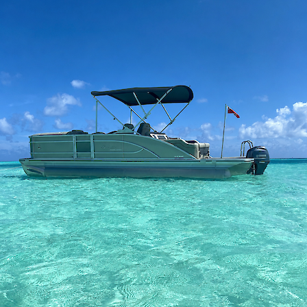 A green pontoon boat floats on clear turquoise water under a bright blue sky with scattered clouds.