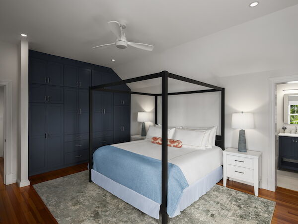 A modern bedroom with a black four-poster bed, blue bedding, large dark blue built-in wardrobes, white nightstands, and a light gray rug.