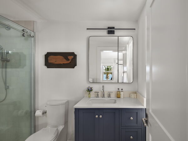 A compact bathroom with a glass shower, a white toilet, a blue vanity, a single mirror above the sink, and minimal decor.
