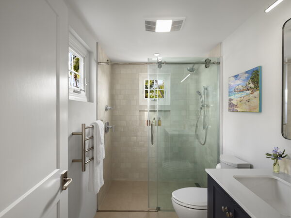 A modern bathroom with a glass shower enclosure, white walls, a tiled floor, a vanity with a dark cabinet, and a small window.