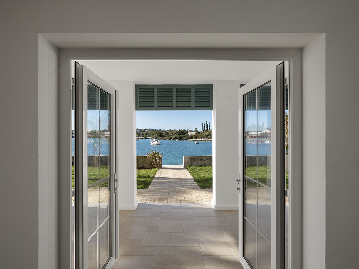 A bright doorway opens to a patio with a view of a blue pool and lush greenery beyond, framed by open glass doors.