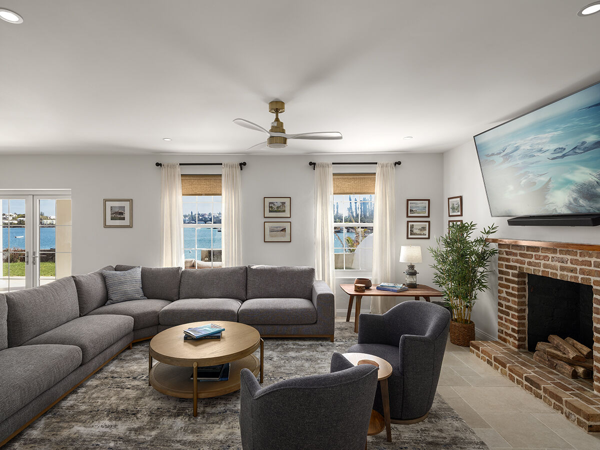 Cozy modern living room with a large gray sectional, two chairs, brick fireplace, a wall-mounted TV, windows, and a round coffee table.
