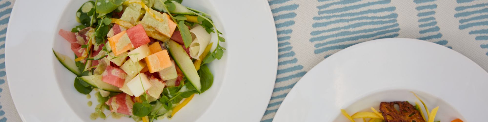 The image shows two plates of salads with various colorful ingredients on a patterned tablecloth, arranged artistically for a meal.