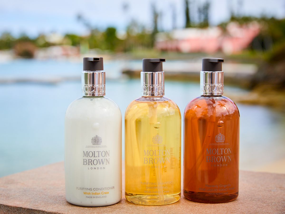 Three bottles of Molton Brown lotion are sitting on a ledge with a scenic, blurred background.