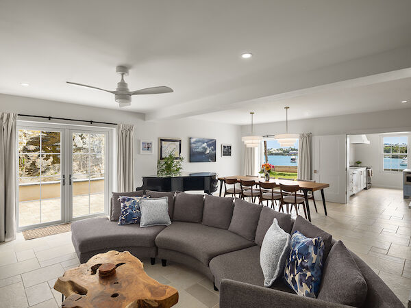Spacious open-plan living area with a gray sectional sofa, wooden coffee table, dining table, ceiling fan, and sliding glass doors to a balcony.