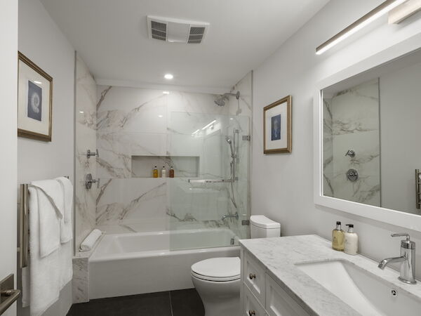 A modern bathroom with a marble-tiled bathtub/shower, white fixtures, a glass shower door, a double vanity, and soft lighting.