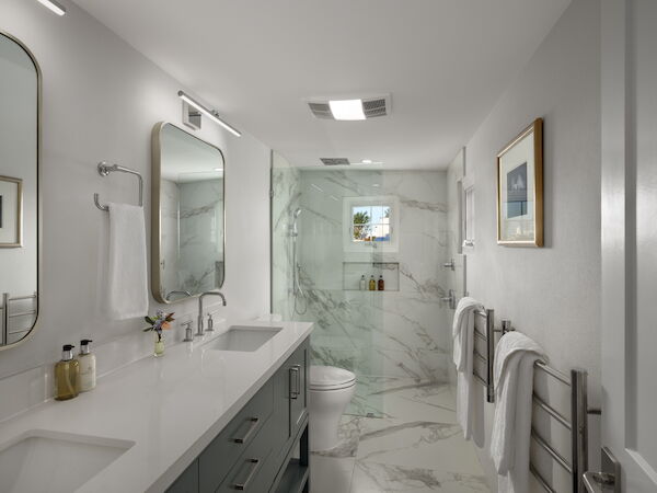 A modern bathroom with a double sink vanity, marble floors, a glass shower enclosure, a toilet, and towels on racks along the wall, neat and bright.