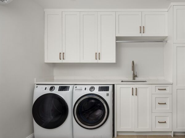 A modern laundry area with white cabinetry, a stainless sink, and a front-load washer and dryer set beneath the counter.
