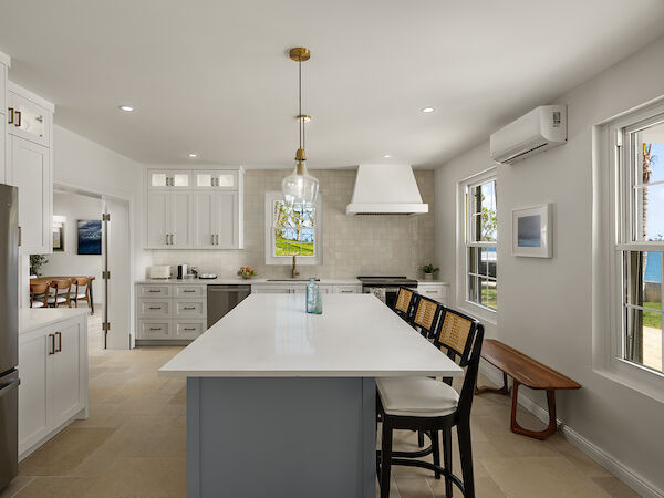 A bright, modern kitchen with a large central island, white cabinetry, pendant lights, and a small bench by the window, airy and clean.