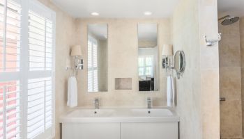 A modern bathroom with dual sinks, mirrors, wall-mounted lights, towels, and a walk-in shower next to it.