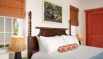 A cozy bedroom with a wooden bed, colorful bedding, green nightstand, two lamps, and bamboo window shades, decorated with a nature-themed wall picture.