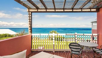 A scenic patio overlooking the ocean, featuring outdoor furniture including loungers and a table with chairs, under a wooden pergola.