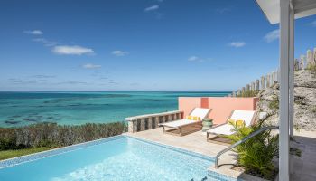 A stunning oceanfront view featuring an infinity pool, lounge chairs, and a clear blue sky, creating a perfect relaxing atmosphere.