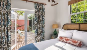 A cozy bedroom with a large bed, decorative pillows, an open door to a patio with outdoor furniture, patterned curtains, and a bedside lamp ending the sentence.