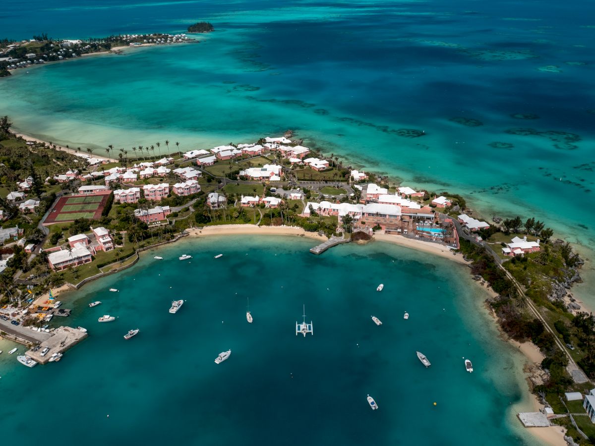 An aerial view of a coastal area with turquoise waters, several boats, and a cluster of buildings surrounded by greenery and sandy beaches.