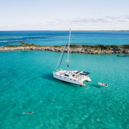 A white sailboat anchored in clear turquoise waters near a rocky shoreline under a blue sky.