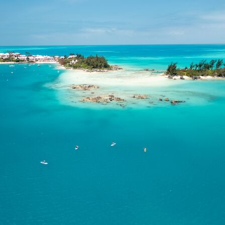 Aerial view of a turquoise lagoon with small sandy beaches, boats near shore, and a distant coastline under a bright blue sky.