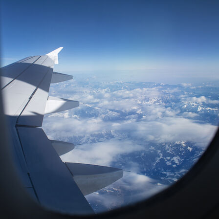 View of an airplane wing and clouds seen from the window, blue sky above, with the aircraft in flight.