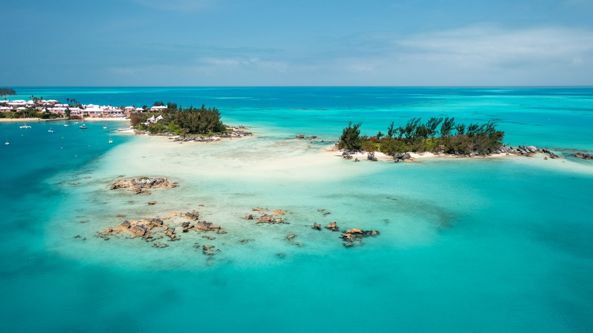 Aerial view of a picturesque island with turquoise water, sandy beaches, and lush greenery under a clear blue sky, perfect for a tropical getaway.