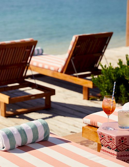 Beachside lounge area with striped sunbeds and a refreshing drink.