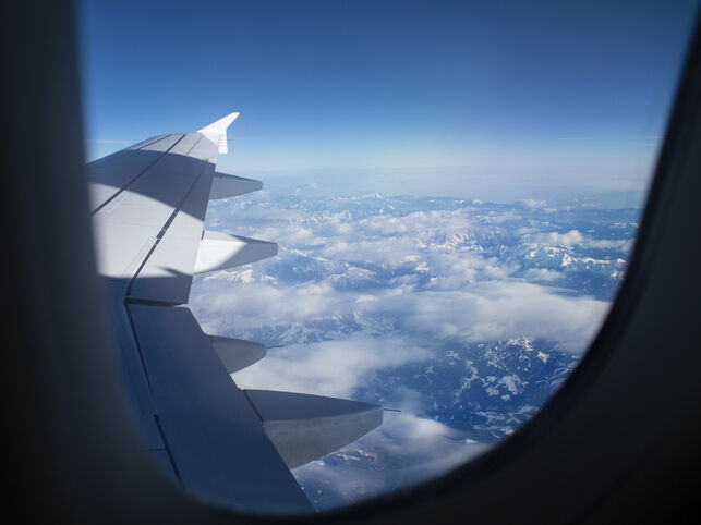 View from an airplane window showing the wing and winglets above clouds stretching over a distant landscape.