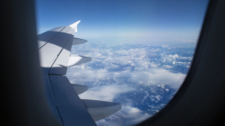 View from an airplane window showing the wing and winglets above clouds stretching over a distant landscape.