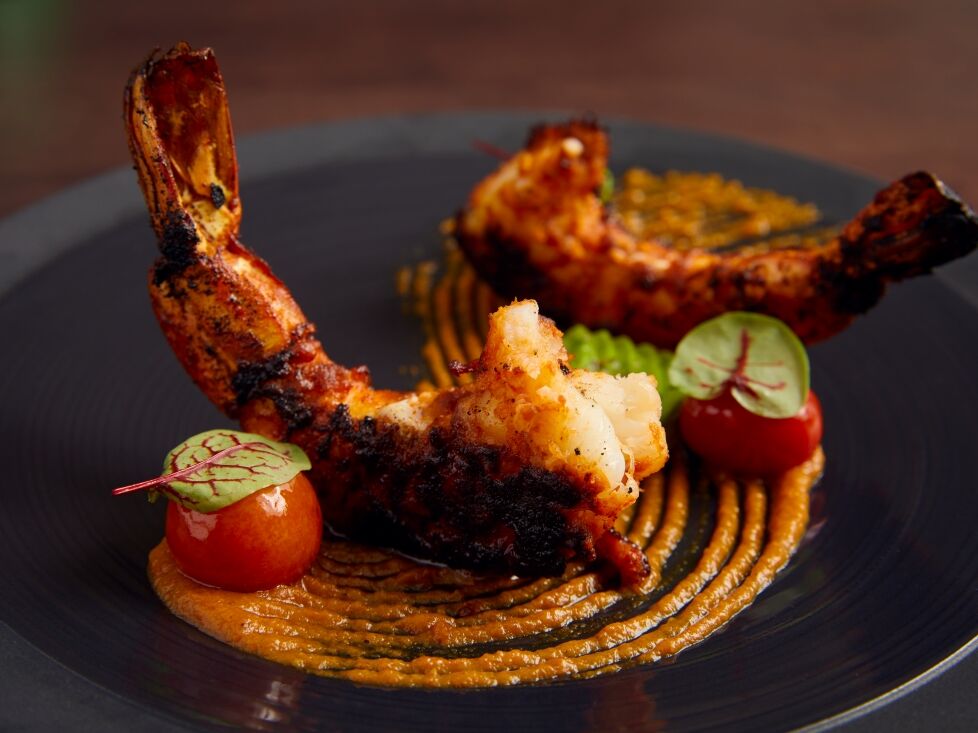 Grilled chicken drumsticks with roasted sausage, tomato halves, and herb garnish on a dark plate.