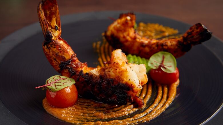 Grilled chicken drumsticks with roasted sausage, tomato halves, and herb garnish on a dark plate.