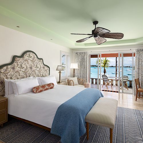 A beautifully decorated bedroom with a king-sized bed, ceiling fan, and a stunning ocean view through sliding glass doors ending the sentence.