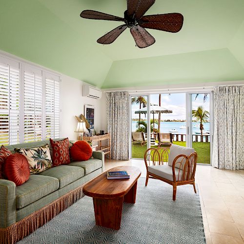 A cozy living room with a green ceiling, comfortable sofa, wooden coffee table, and large windows offering a view of a tropical outdoor space.