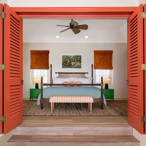 This image shows a cozy bedroom with a four-poster bed, colorful doors, green cabinets, a ceiling fan, and patterned decor.