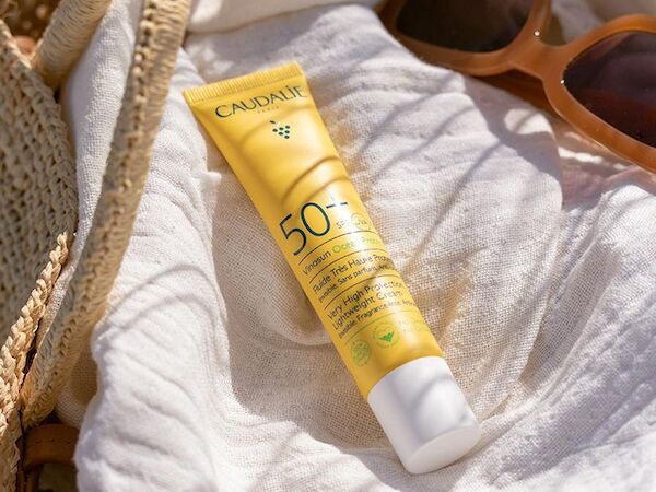 A Caudalie SPF 50 sunscreen tube rests on a white towel with sunglasses nearby.