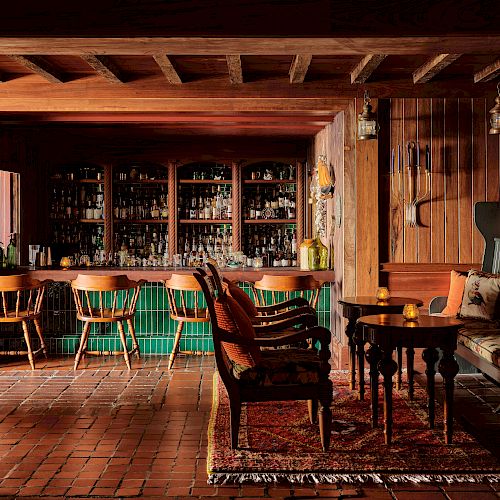 The image shows a cozy, rustic bar with wooden furniture, a well-stocked bar, cushioned seats, and warm lighting, creating an inviting atmosphere.