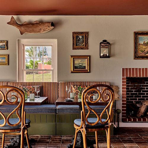 The image shows a cozy dining area with wooden chairs, a table, wall art, a brick fireplace, and a fish sculpture on the wall, creating a rustic atmosphere.