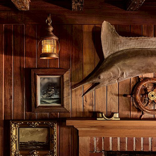 The image shows a wooden-paneled wall with a mounted fish, nautical-themed decor, framed paintings, a lantern, and part of a fireplace.