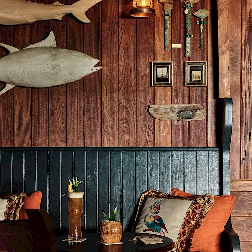 A cozy corner with wooden decor, cushions, drinks on a table, and wall-mounted shark models and frames. A warm lantern light adds to the ambiance.