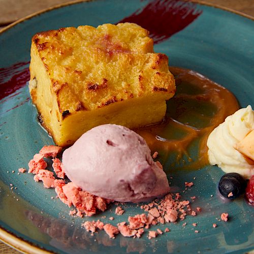 The image shows a dessert plate with a slice of baked pudding, a scoop of purple ice cream, whipped cream, and fresh berries.