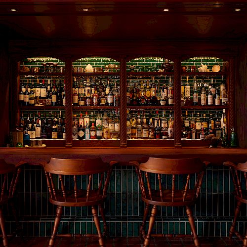 A cozy bar with wooden chairs lined up in front of a fully stocked backbar with various bottles of liquor illuminated softly.