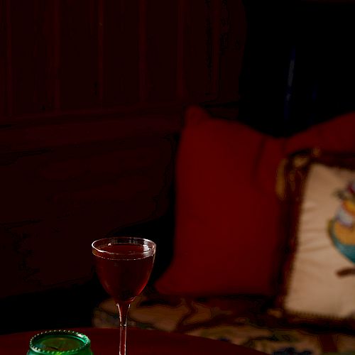 The image shows a cozy setup with a green candle, a book, and a glass of wine on a table, with cushions in the background.