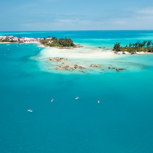 An aerial view of a tropical island surrounded by turquoise water, with boats scattered around and a coastal town visible in the background.